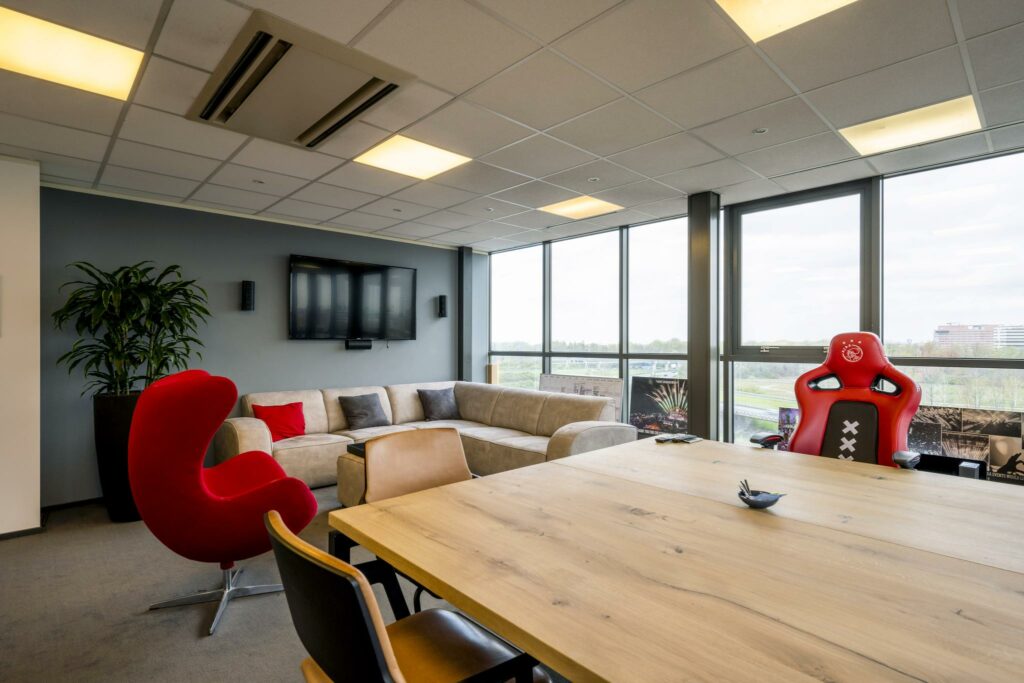 Moderne kantoorruimte aan de Anthony Fokkerweg met loungehoek, vergadertafel en rode bureaustoel met Ajax-logo.